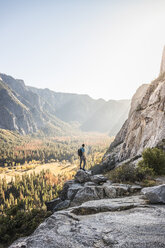 Man on boulder looking out at valley forest, Yosemite National Park, California, USA - CUF07878