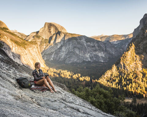 Frau auf einem Felsen mit Blick auf den Wald im Tal, Yosemite-Nationalpark, Kalifornien, USA, lizenzfreies Stockfoto