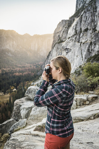 Frau fotografiert Landschaft von einer Felsformation aus, Yosemite National Park, Kalifornien, USA, lizenzfreies Stockfoto