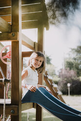 Porträt eines jungen Mädchens, das oben auf einer Parkrutsche sitzt und lächelt - CUF07894