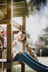 Portrait of young girl, sitting at top of park slide, smiling - CUF07894