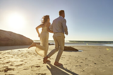 Mature couple running along beach, hand in hand, rear view, Cape Town, South Africa - CUF07903