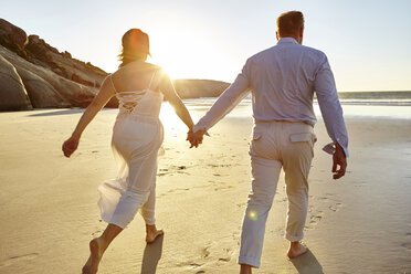 Mature couple walking along beach, hand in hand, rear view, Cape Town, South Africa - CUF07908