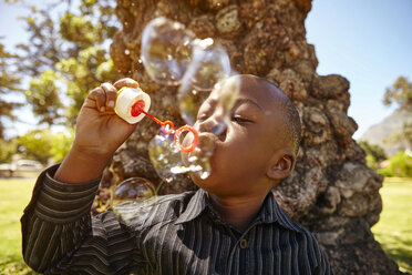Boy blowing bubbles in park - CUF07936