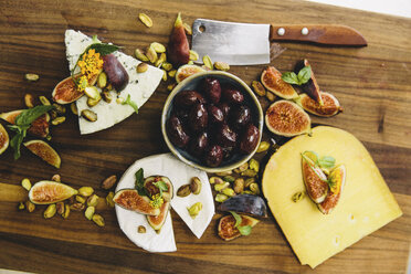 Variety cheese plate with figs, olives, pistachios, cleaver on wooden chopping board - ISF01680