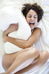Draufsicht auf eine nackte Frau, die auf einem Bett liegt und sich an ein Kissen schmiegt - ISF01710