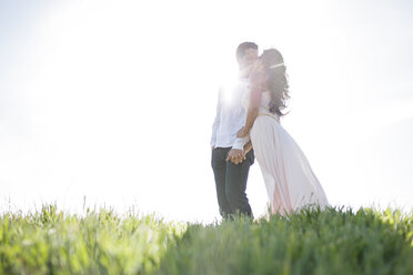 Romantisches Paar, das sich auf einem grasbewachsenen Hügel im Sonnenlicht küsst - ISF01711