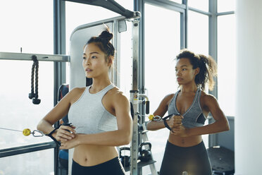 Zwei junge Frauen trainieren in einem Fitnessstudio und benutzen Fitnessgeräte - ISF01724