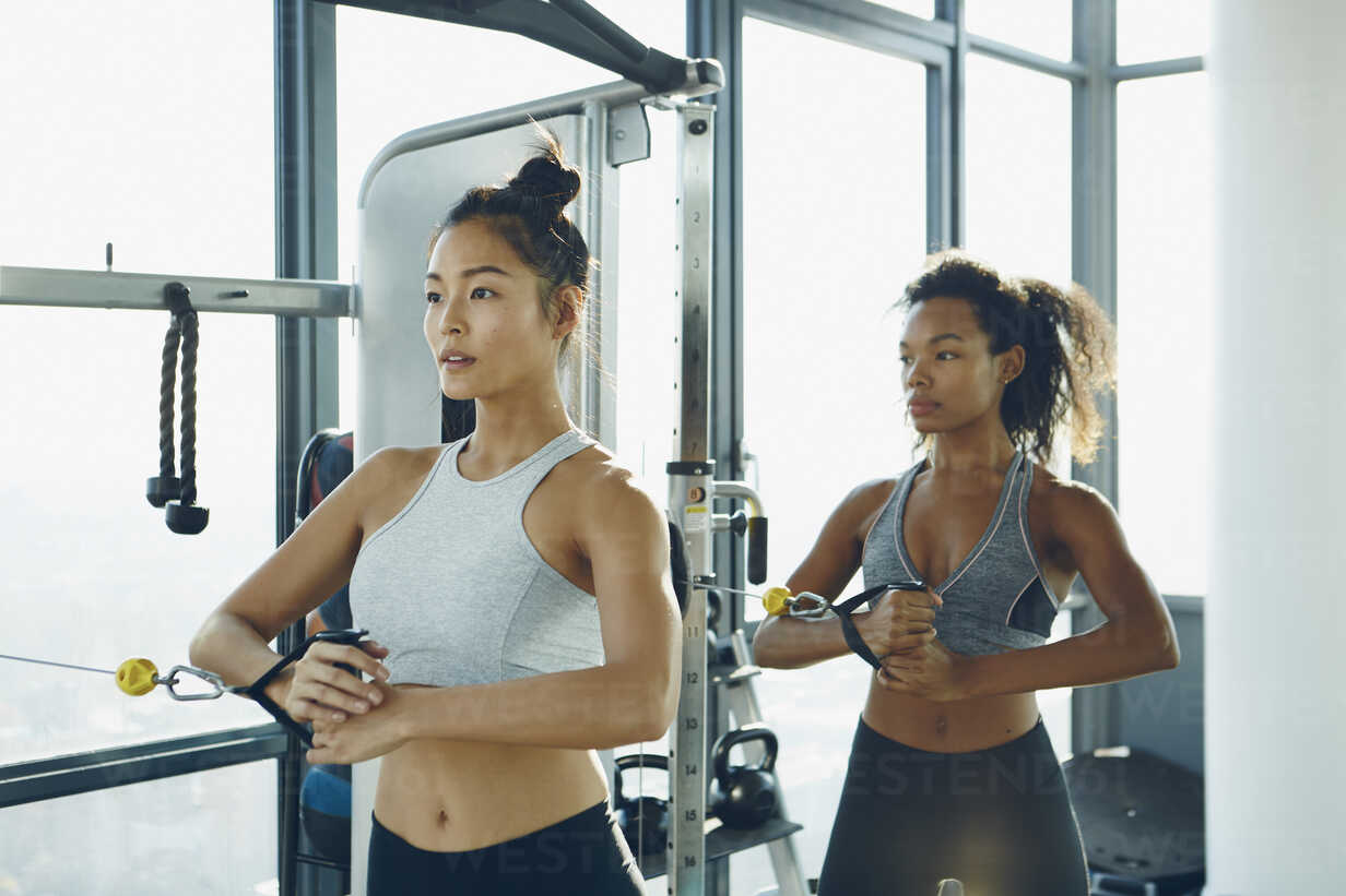 Two young women working out in gym, using gym equipment stock photo