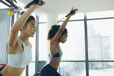 Zwei junge Frauen trainieren in einem Fitnessstudio und benutzen Fitnessgeräte - ISF01726