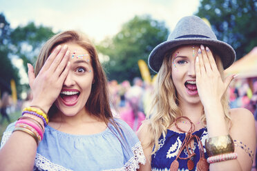 Portrait of two young female friends covering an eye at festival - ISF01765