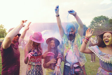 Young adult friends dancing and throwing coloured chalk powder at festival - ISF01782