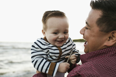 Vater am Strand hält lächelnden kleinen Jungen - ISF01807