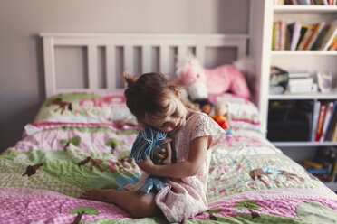 Mädchen sitzt auf einem Bett und umarmt eine Stoffpuppe - ISF01822