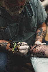 Tattooist tattooing young man's arm - ISF01851