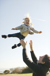 Weibliches Kleinkind, das von seinem Vater in die Luft geworfen wird, vor blauem Himmel - ISF01861