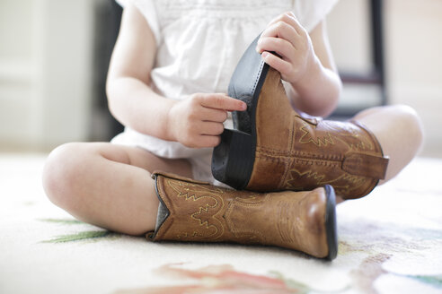 Blick von unten auf ein weibliches Kleinkind, das auf dem Boden sitzt und Cowboystiefel trägt - ISF01877
