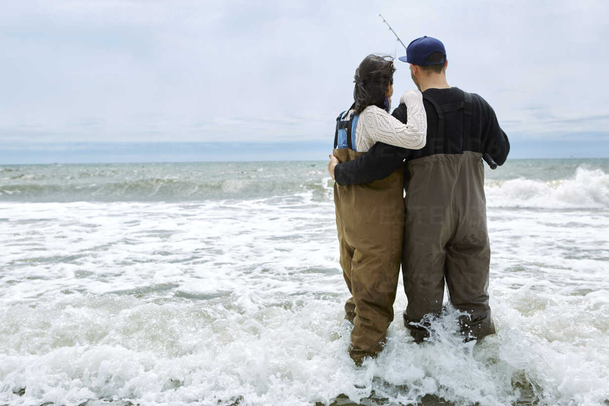 Rear view of young couple in waders sea fishing stock photo