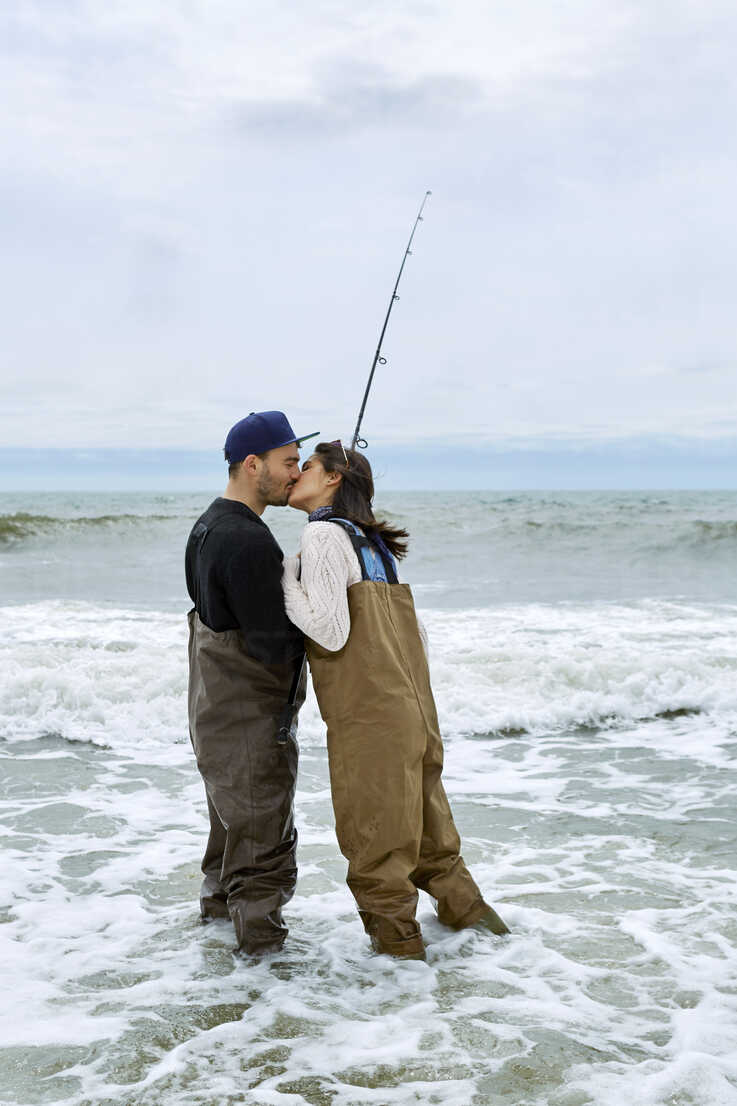 Young woman in waders casting sea fishing rod from beach stock photo