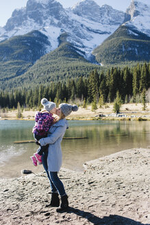 Mutter hält und küsst Tochter am Flussufer, Three Sisters, Rocky Mountains, Canmore, Alberta, Kanada - ISF01939