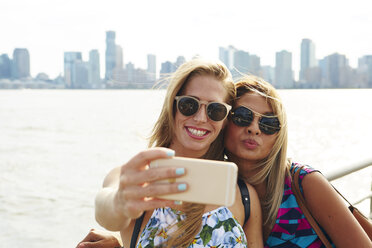 Zwei Frauen machen ein Smartphone-Selfie am Wasser mit Skyline, New York, USA - ISF01944