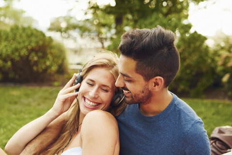 Junge Frau und Mann hören Kopfhörer-Musik im Park, lizenzfreies Stockfoto