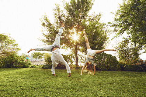 Male and female adult friends doing cartwheels in park stock photo