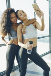 Zwei junge Frauen im Fitnessstudio, die ein Selfie machen und ein Smartphone benutzen - ISF02032