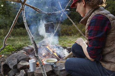 Woman sitting beside camp fire, cooking food, Colgate Lake Wild Forest, Catskill Park, New York State, USA - ISF02035