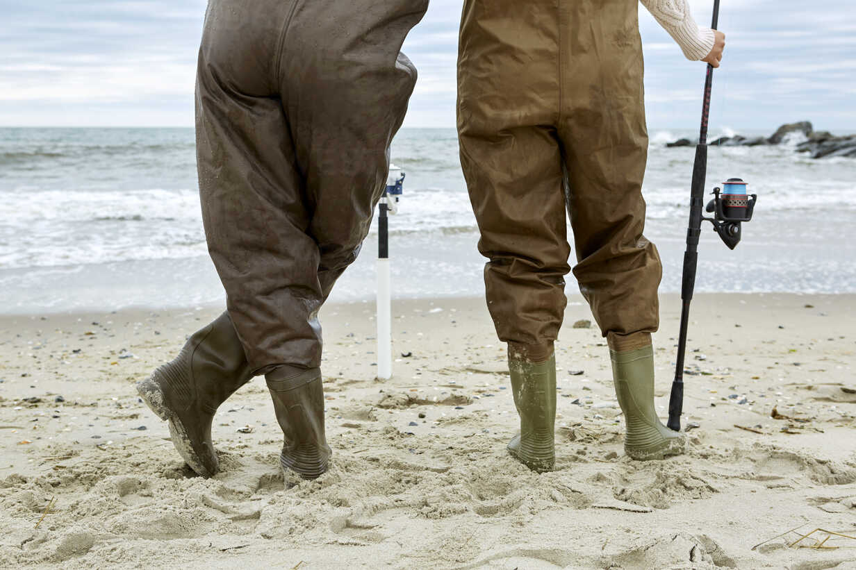 Waist down rear view of young couple in sea fishing waders on beach stock  photo