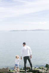 Rückansicht eines reifen Mannes und seiner Tochter am Wasser an der Küste - ISF02069