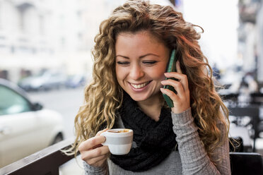 Woman in cafe holding espresso cup making telephone call smiling - CUF08238