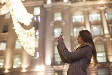 Young woman photographing Christmas lights, Regent Street, London, UK - CUF08247