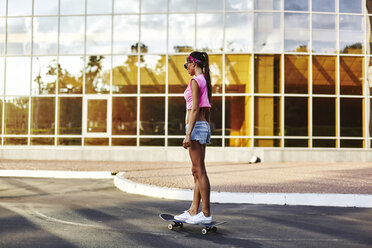 Young woman skateboarding along road - CUF08267