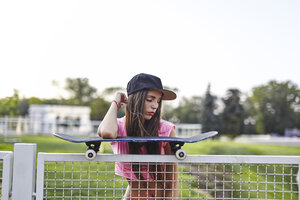 Junge Frau balanciert Skateboard auf Metallzaun, Ellenbogen auf Skateboard - CUF08275