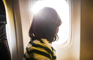 Junge im Flugzeug blickt durch ein sonnendurchflutetes Fenster - CUF08280