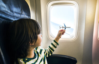 Junge spielt mit Spielzeugflugzeug am Flugzeugfenster - CUF08282