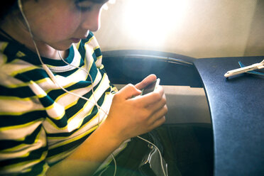 Ausgeschnittene Aufnahme eines Jungen im Flugzeug, der Musik auf einem mp3-Player auswählt - CUF08283