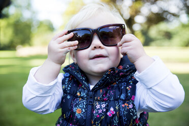 Portrait of female toddler putting on sunglasses in park - CUF08324