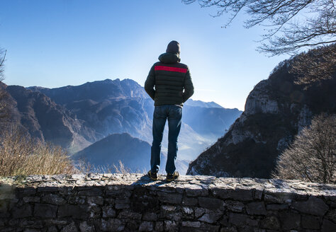 Man standing on wall, looking at mountain view, rear view, Italy - CUF08369