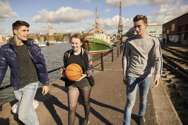 Drei Freunde gehen am Fluss entlang, junge Frau trägt Basketball, Bristol, UK - CUF08383