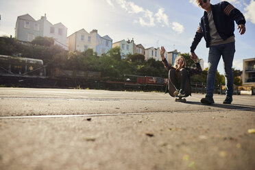 Zwei Freunde albern herum, ein junger Mann zieht eine junge Frau auf einem Skateboard mit, Bristol, UK - CUF08386