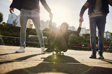 Drei Freunde, die im Freien herumalbern, junge Männer, die eine junge Frau auf einem Skateboard mitziehen, Bristol, UK - CUF08389