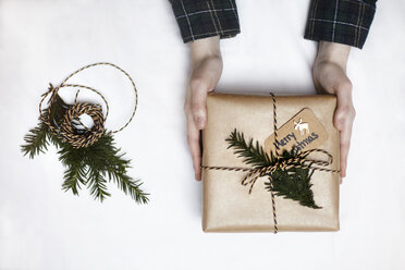 Frau hält ein in braunes Papier eingewickeltes, mit Farn und Schnur verziertes Weihnachtsgeschenk, Draufsicht - CUF08399