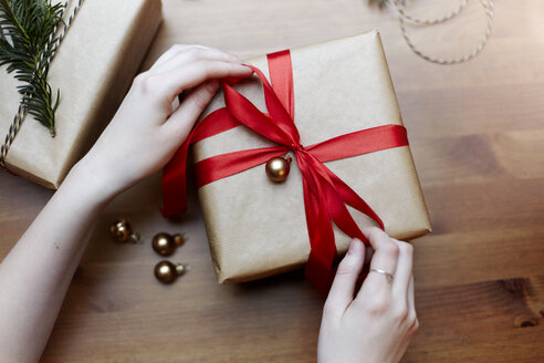 Frau bindet rote Schleife an Weihnachtsgeschenk, Draufsicht - CUF08401