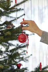 Ältere Frau, die eine Christbaumkugel auf den Weihnachtsbaum steckt - CUF08406