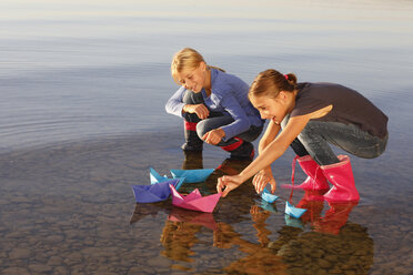Two young girls floating paper boats on water - CUF08427