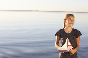 Young girl, standing near water, holding toy boat - CUF08430