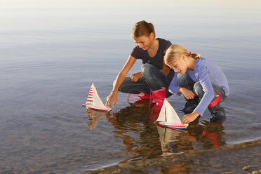 Two young girls floating toy boats on water - CUF08432