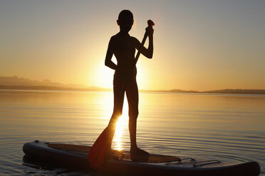 Young girl paddle boarding on water, at sunset - CUF08438